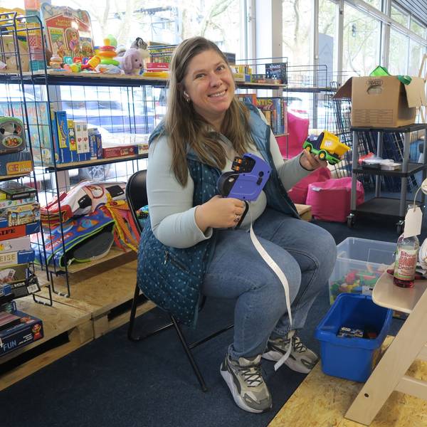 Eine Frau sitzt auf einem Stuhl zwischen Regalen voller Kinderspielzeug.