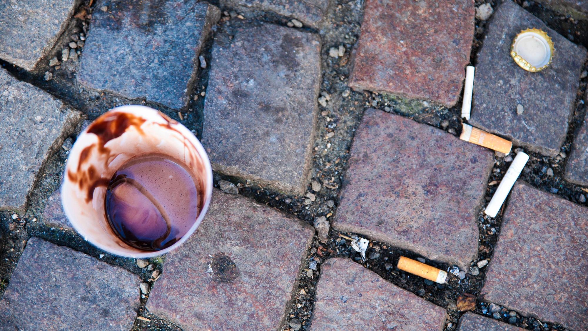 Ein Kaffeebecher steht auf Pflastersteinen.