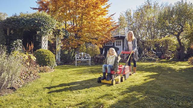 Mutter und Tochter mit einem Rasenmäher im Garten