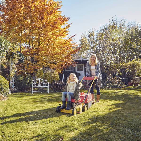 Mutter und Tochter mit einem Rasenmäher im Garten