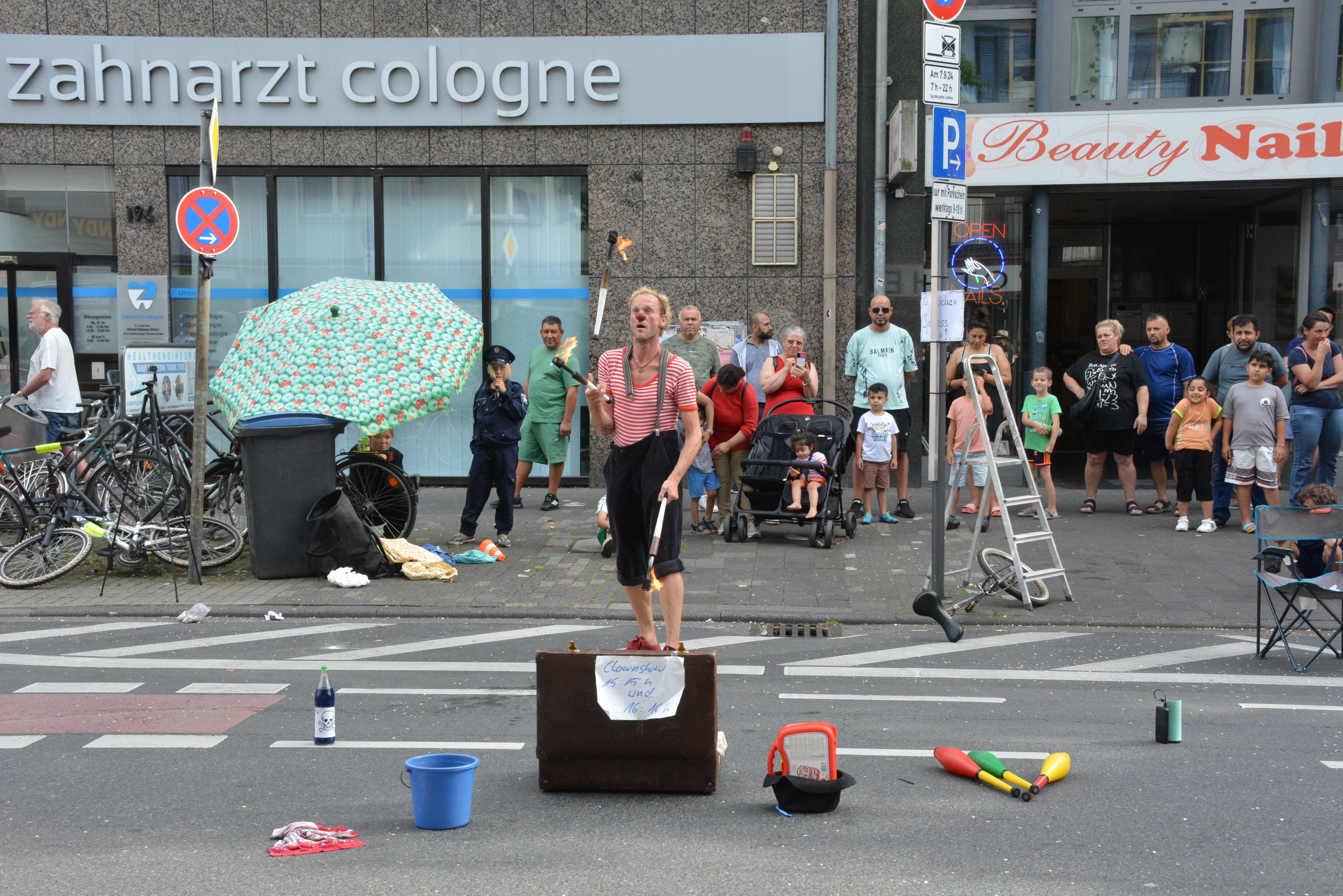 Ein Mann im Clowns-Kostüm jongliert vor Publikum mit Fackeln.