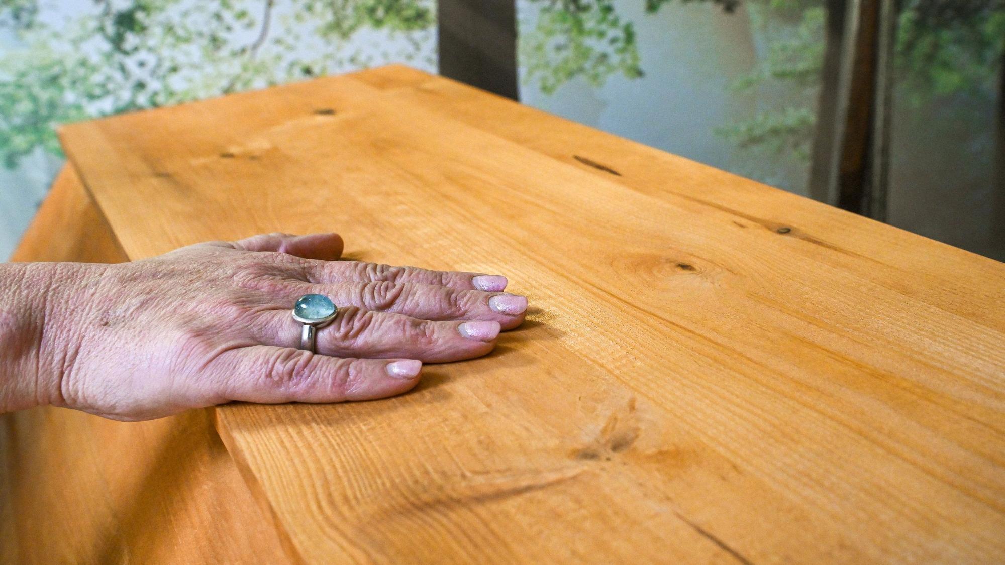 Eine Frau steht an einem Sarg und hat die Hand darauf gelegt.