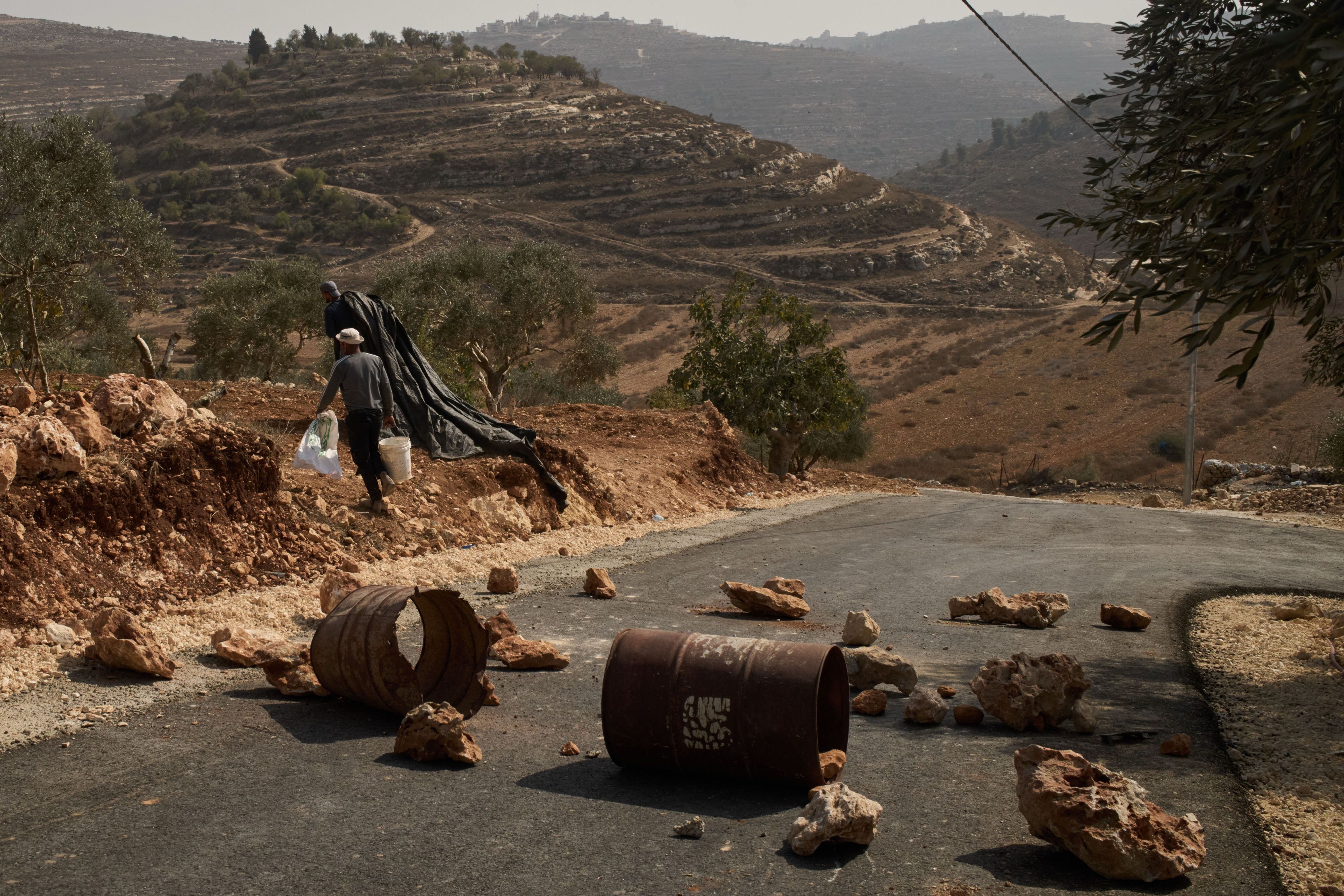 Palästinensische Männer gehen an einer gesperrten Straße vorbei, die errichtet wurde, um israelische Siedler am Betreten des Gebiets zu hindern. Sie wollen die Ernte aus dem Olivenhain einbringen.