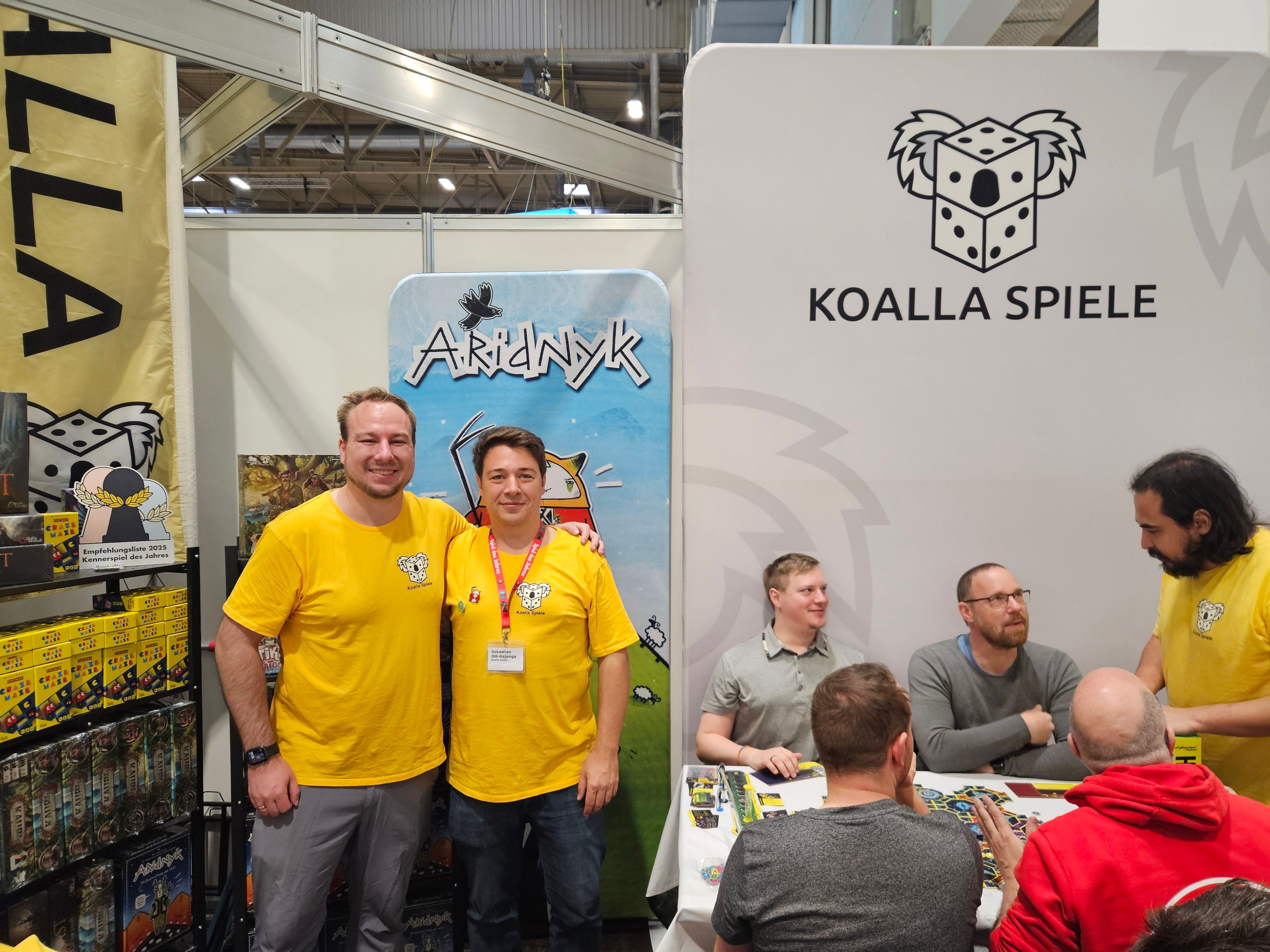 Zwei Spieleentwickler aus Bergisch Gladbach stehen vor einer Infowand auf der Spielemesse in Essen.