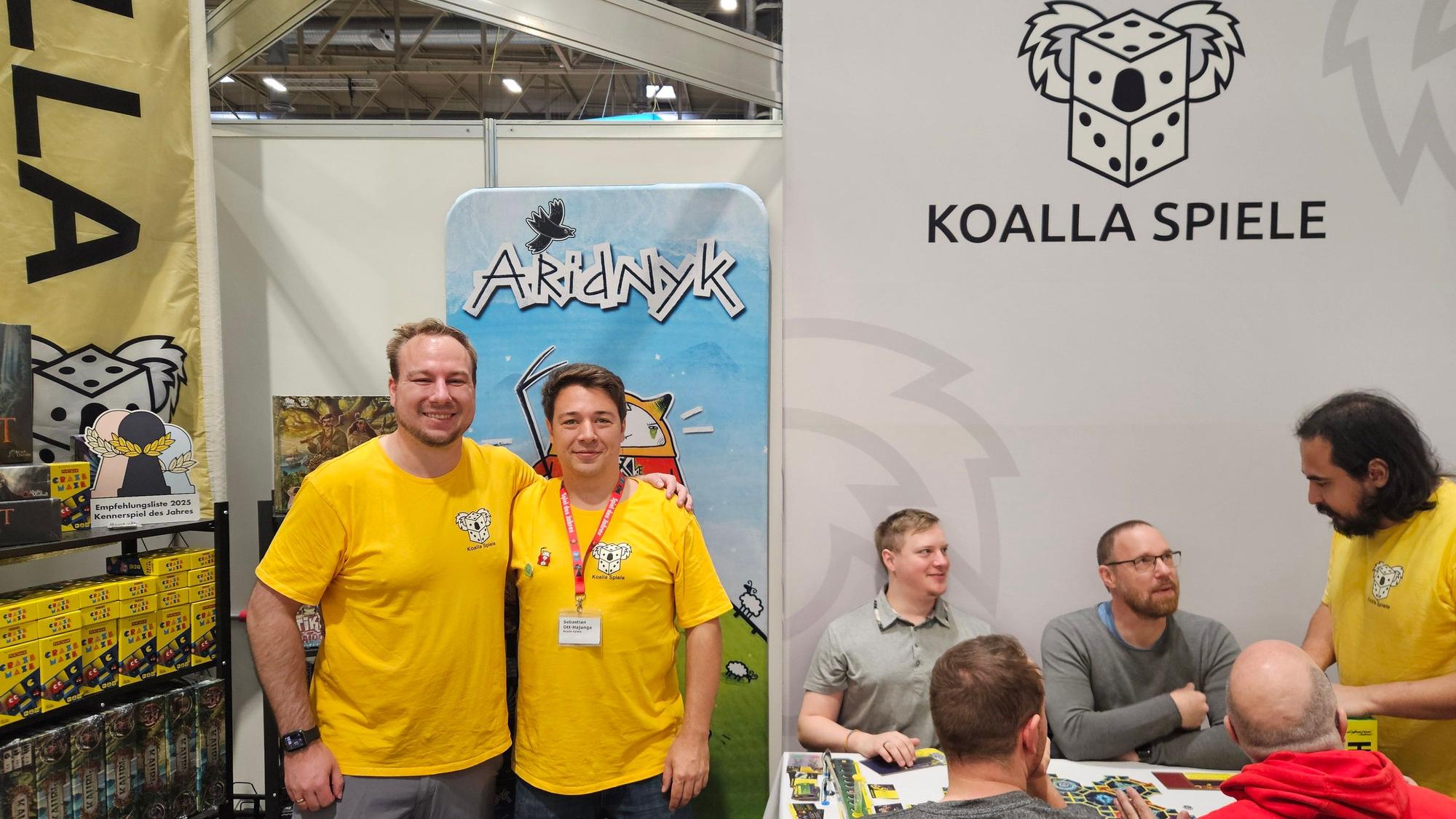 Zwei Spieleentwickler aus Bergisch Gladbach stehen vor einer Infowand auf der Spielemesse in Essen.