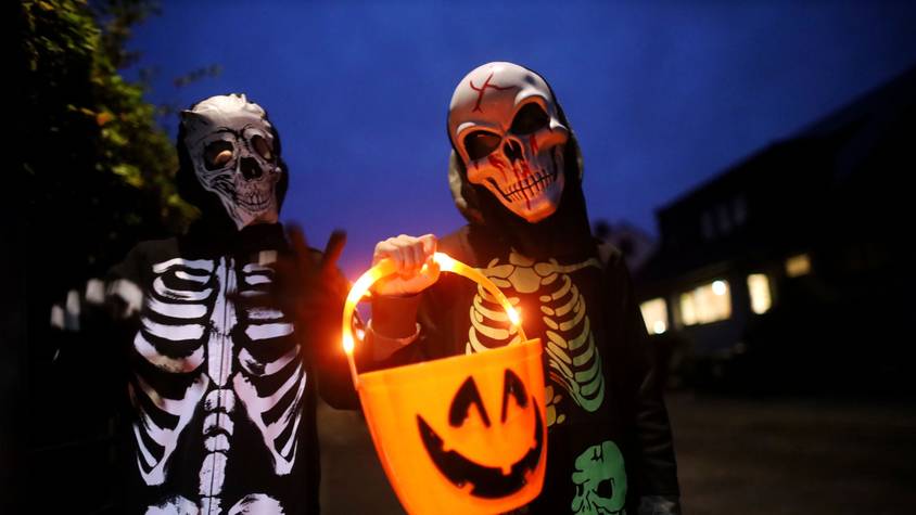Zwei als Skelett verkleidete Kinder tragen einen leuchtenden Halloween-Eimer.