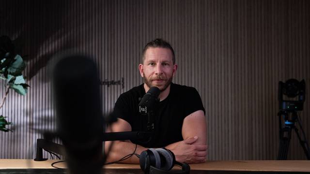 Ein Mann sitzt vor einem Mikrofon und blickt freundlich in die Kamera.