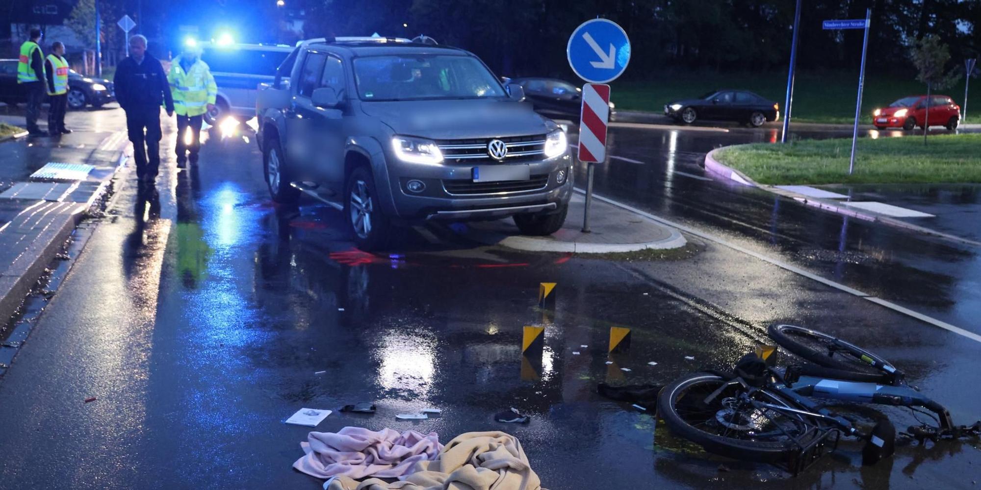 Im Dunkeln steht ein Auto halb auf einer Verkehrsinsel, ein Pedelec-Rad liegt auf dem Boden, Decken daneben. Im Hintergrund leuchtdn die Polizeisirenen blau.