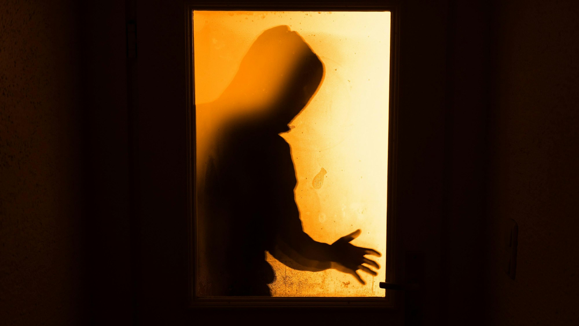 Das Bild ist ein Symbolfoto und zeigt den Schatten einer Person hinter einer Türe.