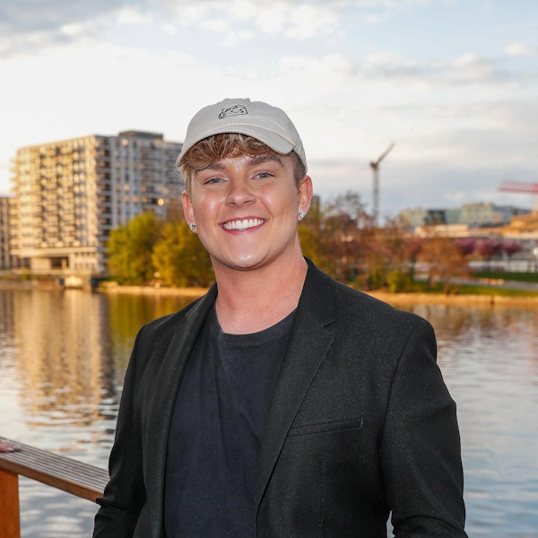 Twenty4Tim steht an einem Gewässer und lacht.