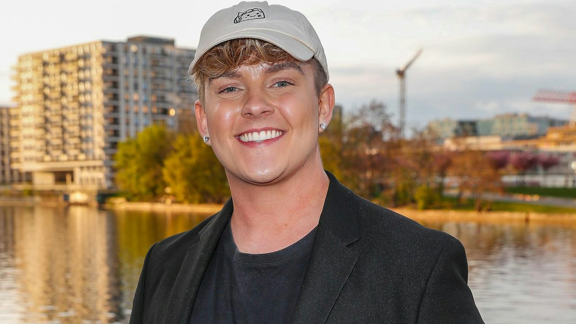 Twenty4Tim steht an einem Gewässer und lacht.