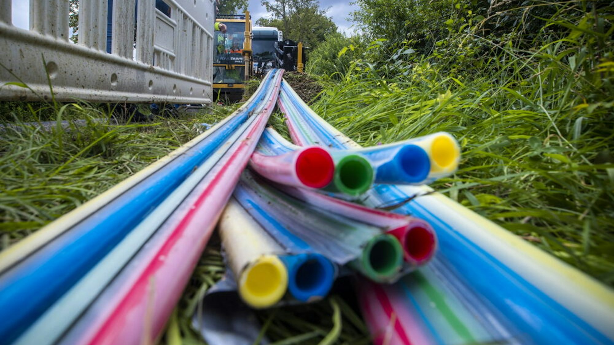 Bunte Kabelhülsen liegen im Gras, im Hintergrund stehen Bagger.