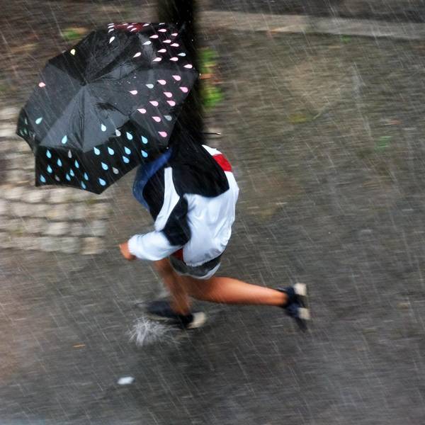 Frau rennt bei einem Sommergewitter mit Schirm herum
