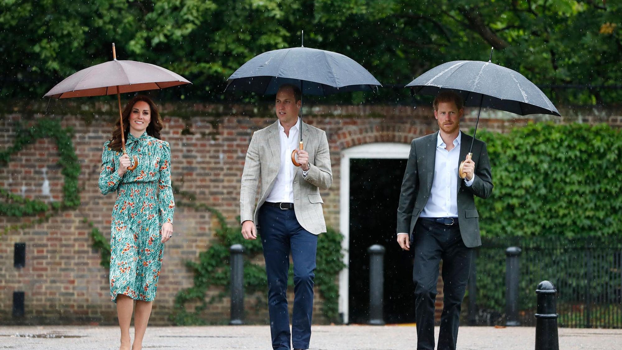 William, Harry und Kate gehen nebeneinander mit Schirmen.