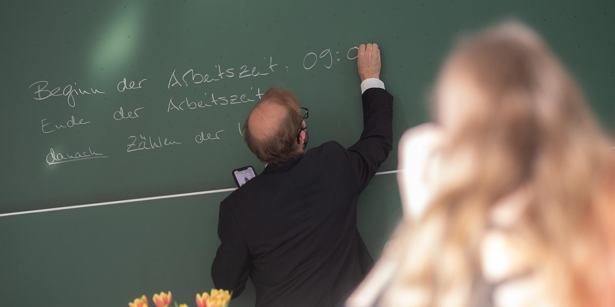 Ein Lehrer schreibt etwas an die Tafel.