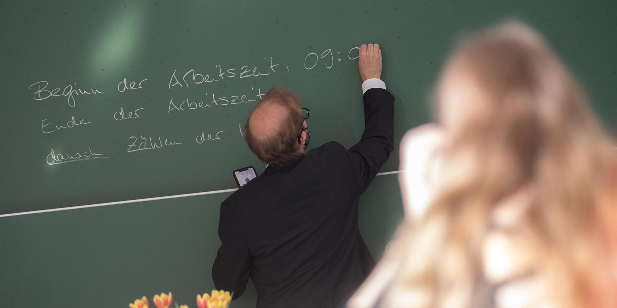Ein Lehrer schreibt etwas an die Tafel.