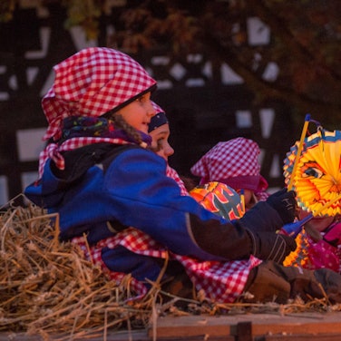 Kinder sitzen im Stroh mit bunten Sonne-, Mond- und Sterne-Laternen.