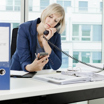 Frau im Büro guckt auf Handy
