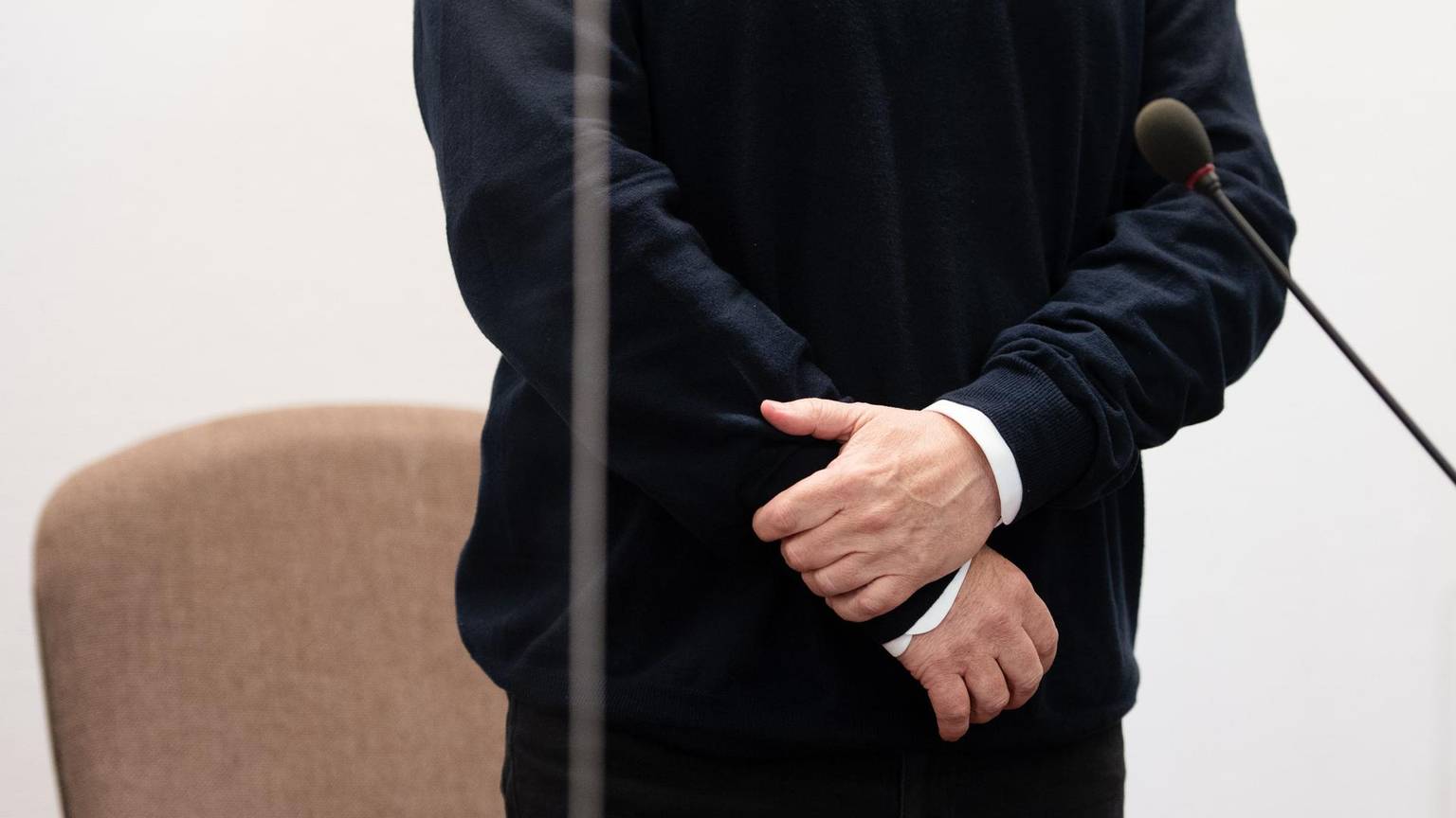 Mit verschränkten Armen steht der Angeklagte vor seinem Stuhl.