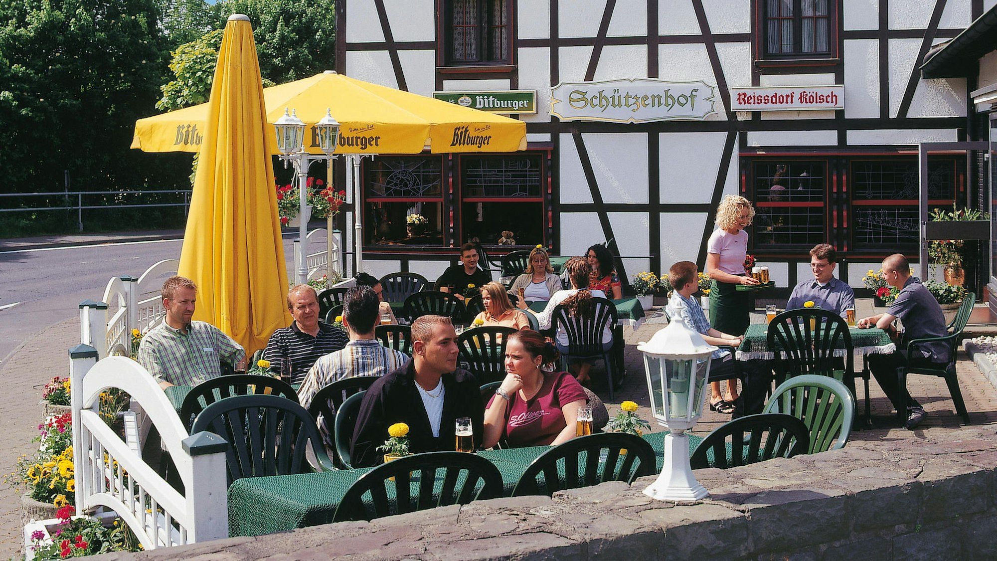 Menschen sitzen auf einer Terrasse vor einem Fachwerkhaus mit dem Schild „Schützenhof“.