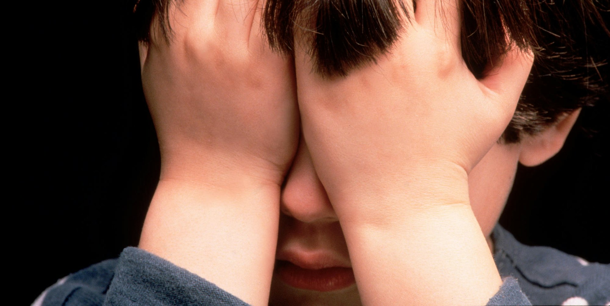 Kind hält sich die Hände vor das Gesicht.