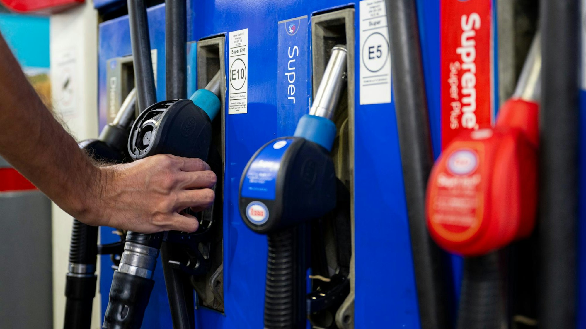 Das Bild zeigt einen Mann, der an einer Tanksäule zur Zapfpistole greift.