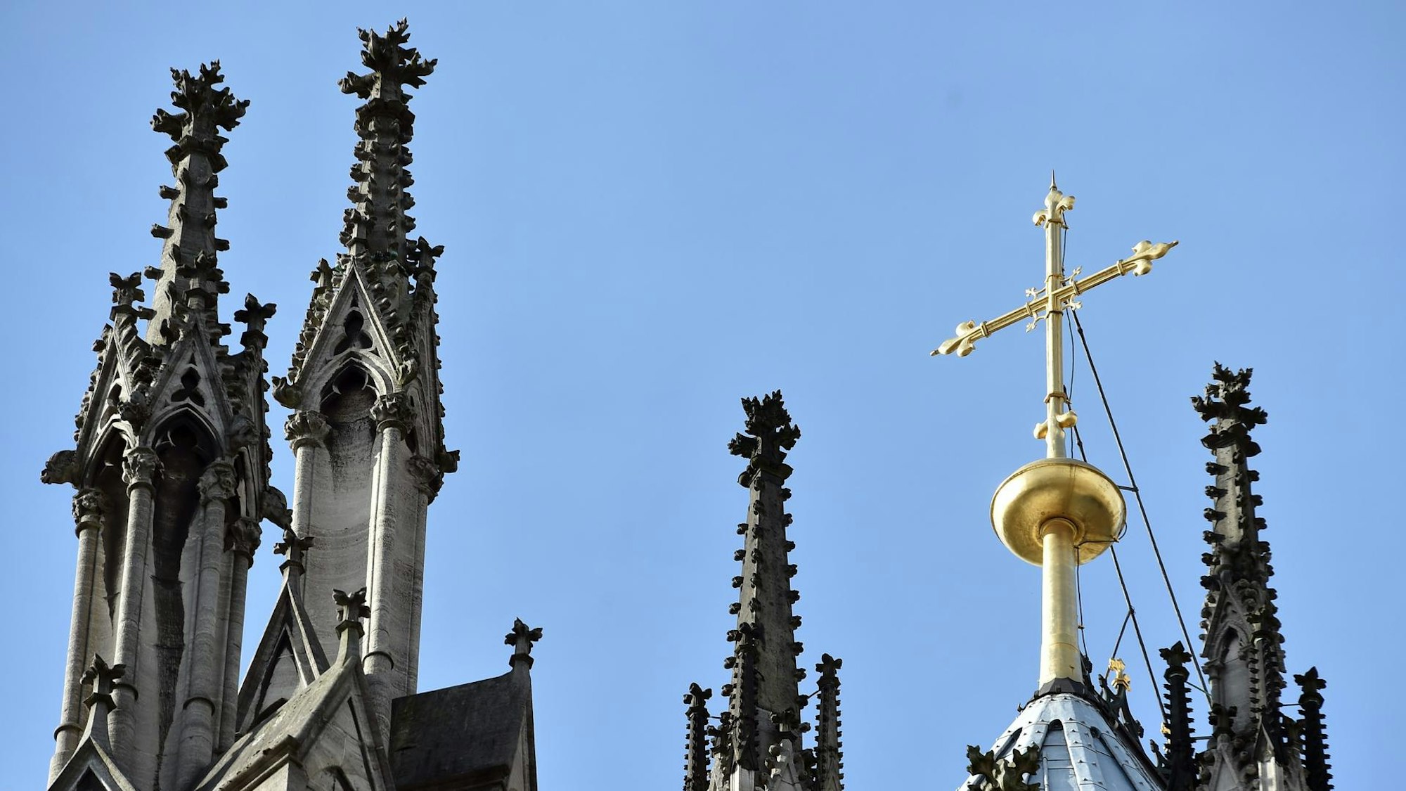 Ein goldenes Kreuz auf dem Kölner Dom leuchtet in der Sonne.