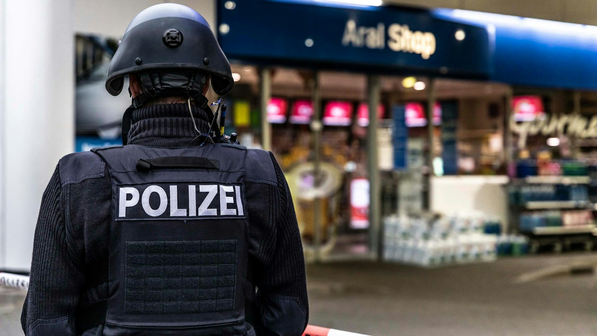 Das Bild zeigt eine Tankstelle, vor der eine Polizistin steht.