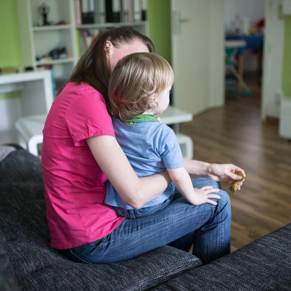 Eine Frau sitzt im Wohnzimmer und hält ein kleines Kind auf dem Schoß.