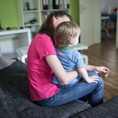 Eine Frau sitzt im Wohnzimmer und hält ein kleines Kind auf dem Schoß.