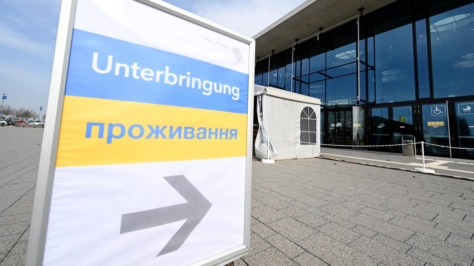 Ein Schilt mit ukrainischer Flagge und der Aufschrift Unterbringung zeigt auf ein Glasgebäude.