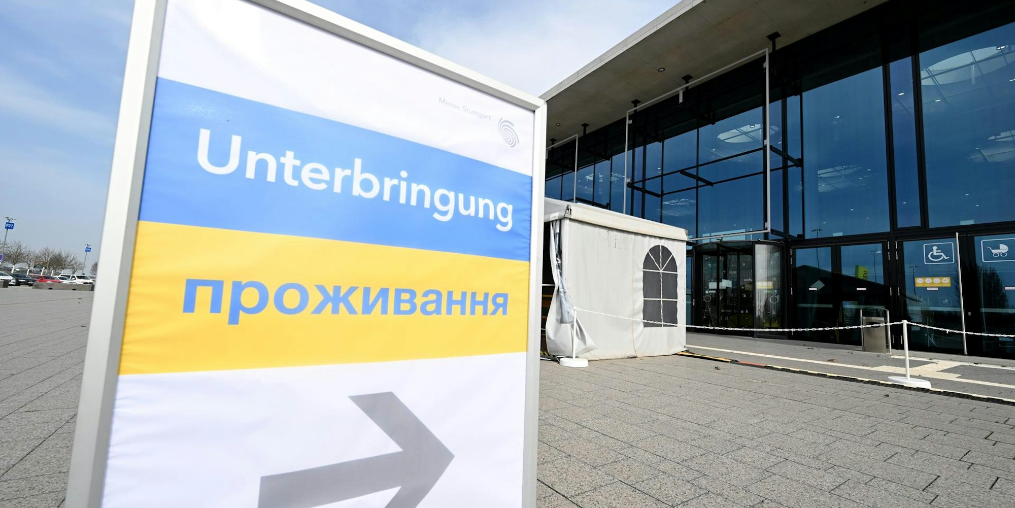 Ein Schilt mit ukrainischer Flagge und der Aufschrift Unterbringung zeigt auf ein Glasgebäude.