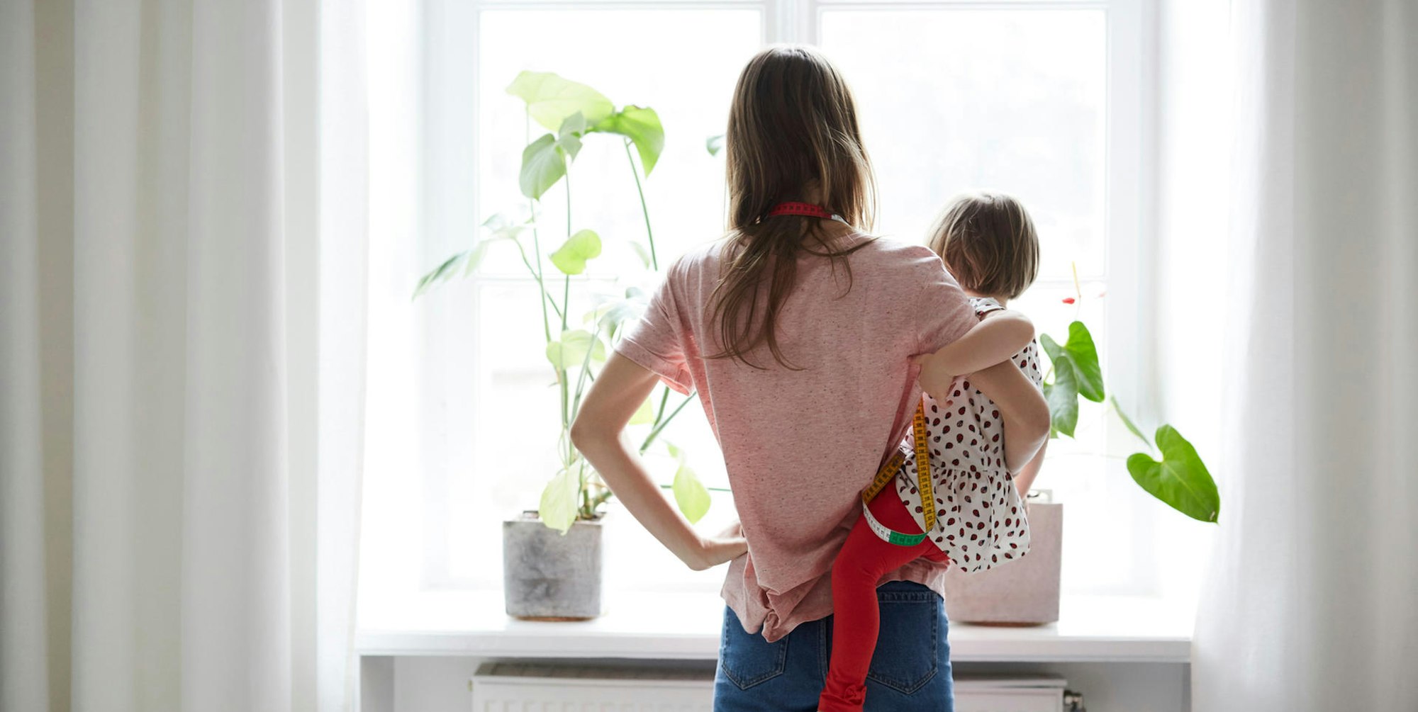 Eine Frau mit Kleinkind auf dem Arm schaut zum Fenster hinaus.