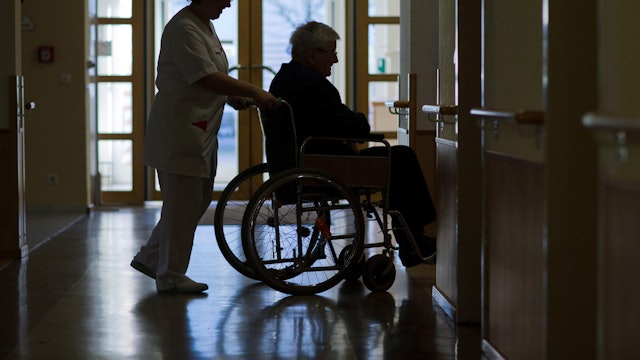Eine Pflegerin schiebt einen älteren Mann im Rollstuhl.
