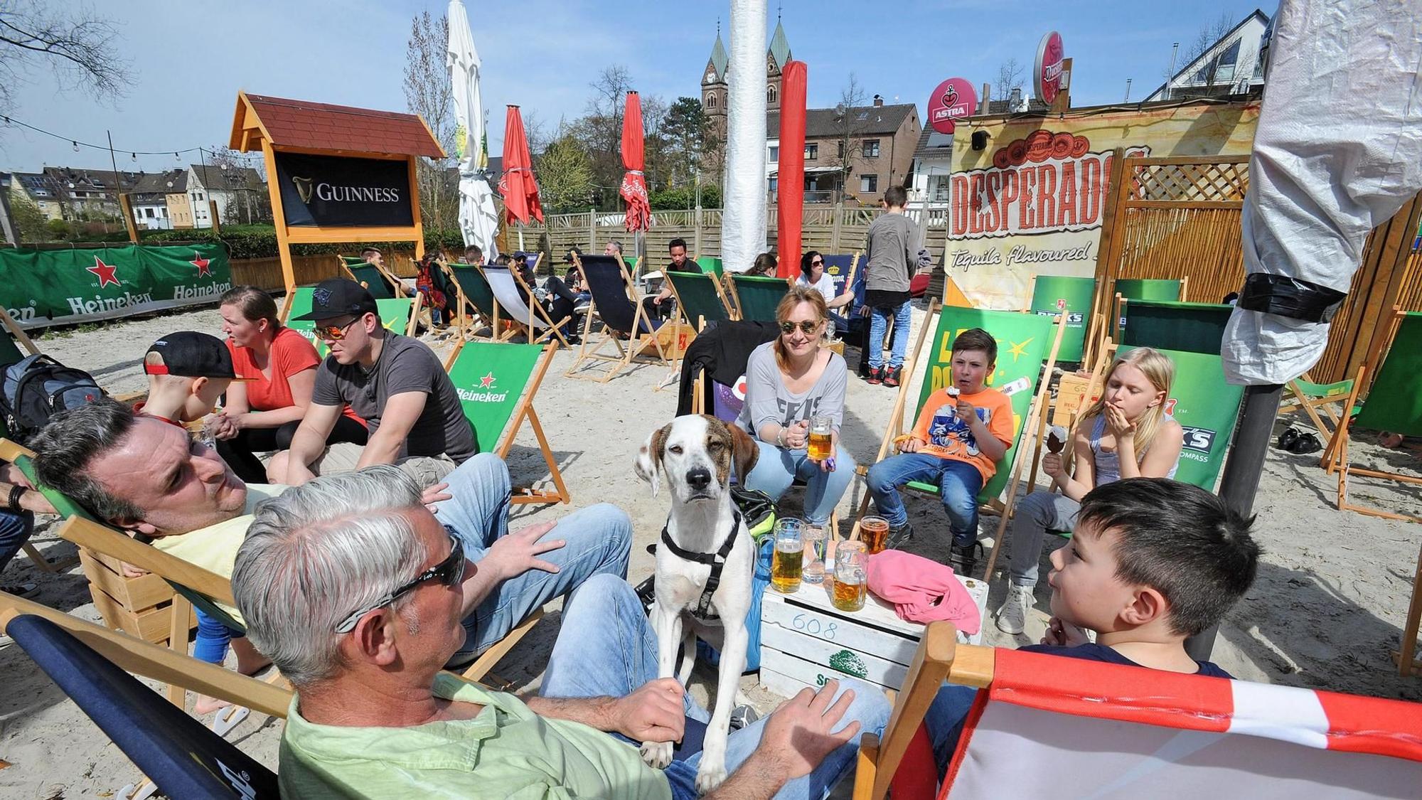 In Liegestühlen im Sand liegen Menschen an der Hitdorfer Fähre