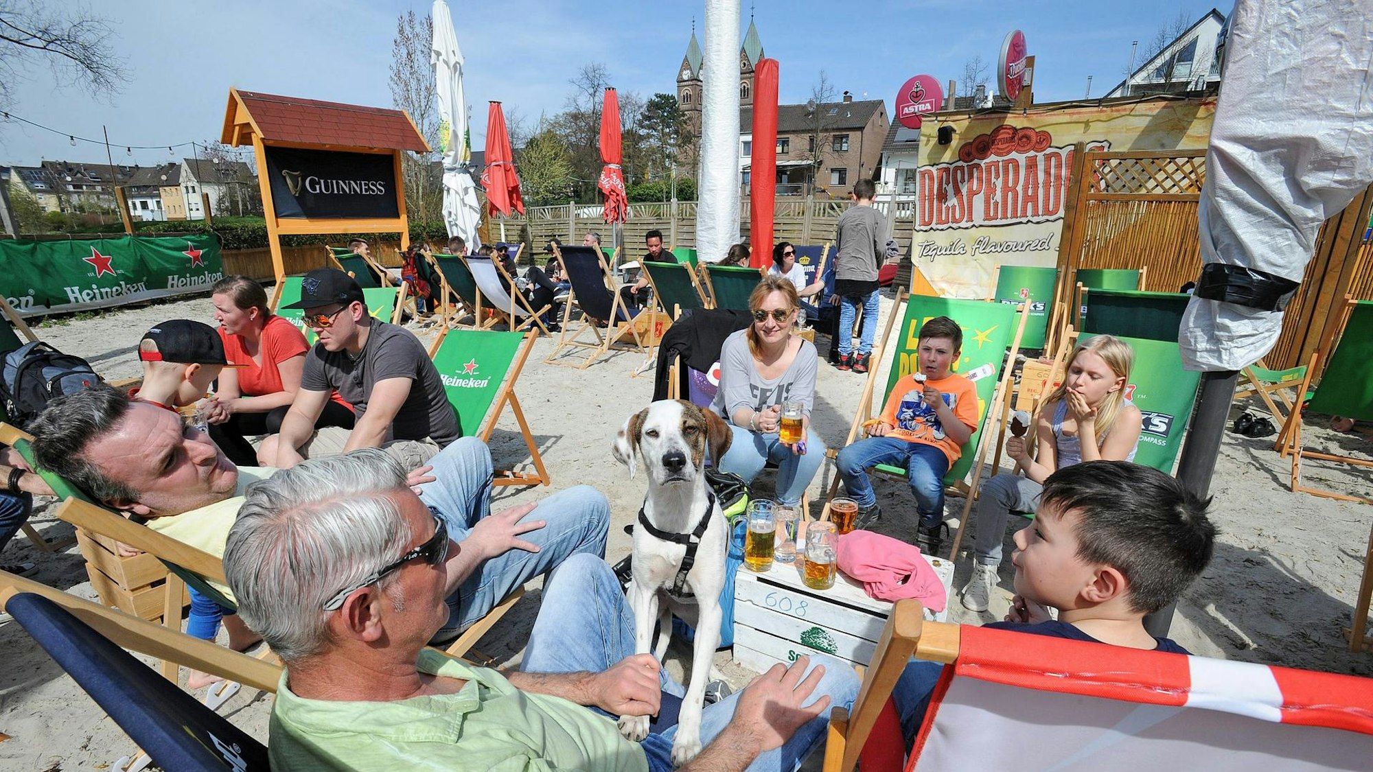 In Liegestühlen im Sand liegen Menschen an der Hitdorfer Fähre
