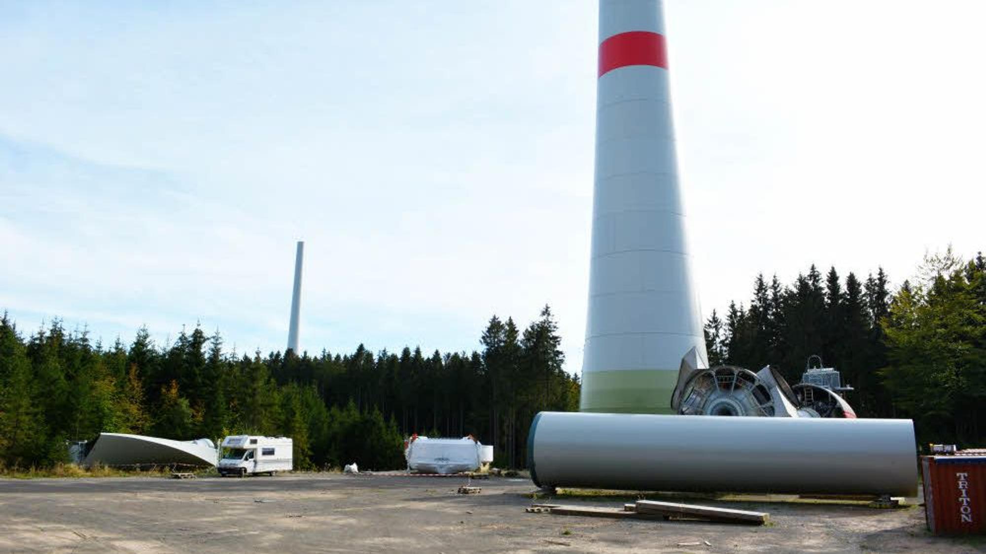 Der untere Teil einer Windkraftanlage mit einem roten Streifen ist zu sehen. Am Boden liegen weitere Bauteile.