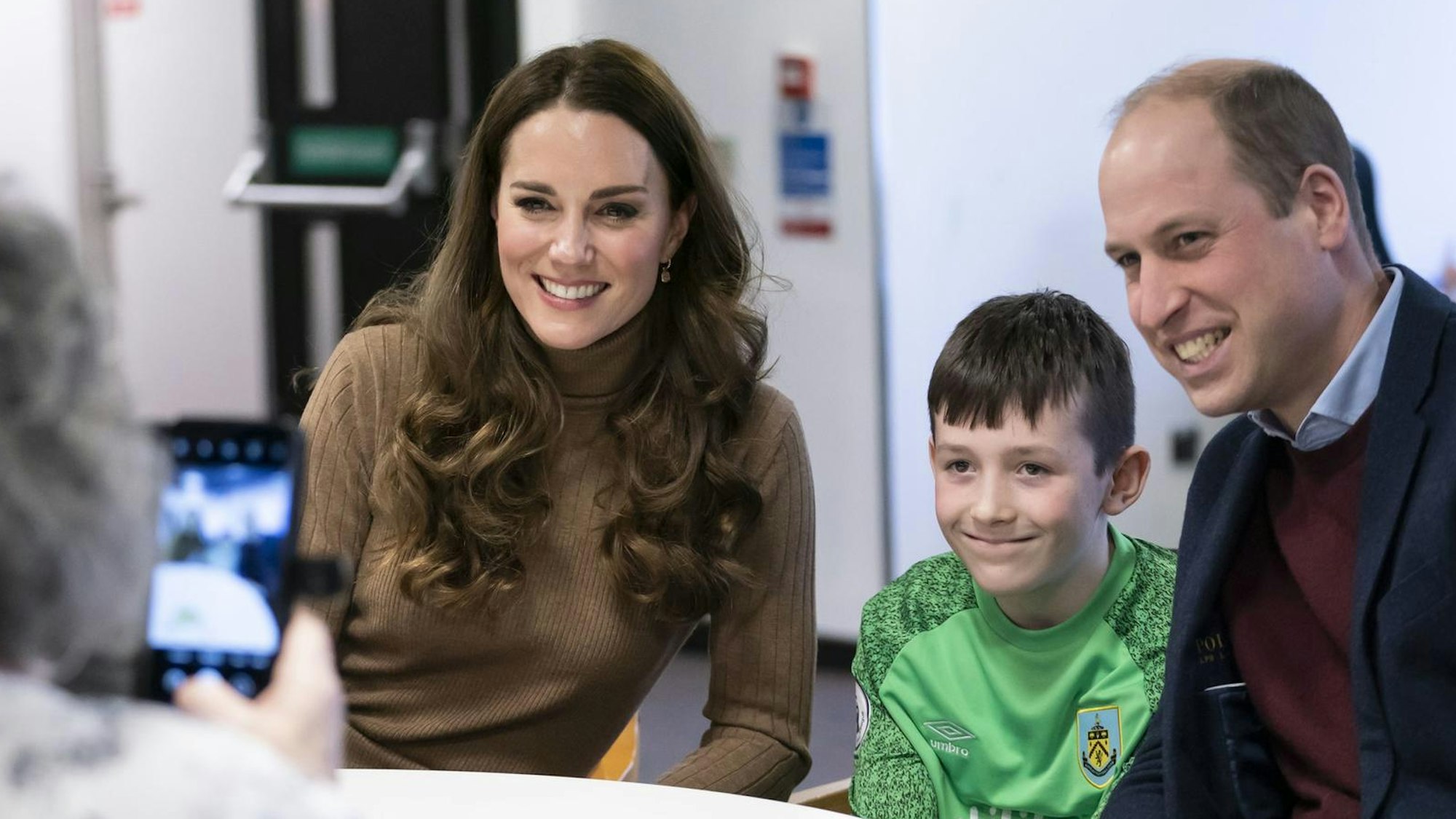 Prinzessin Kate und Prinz William posieren für ein Foto mit einem Kind.