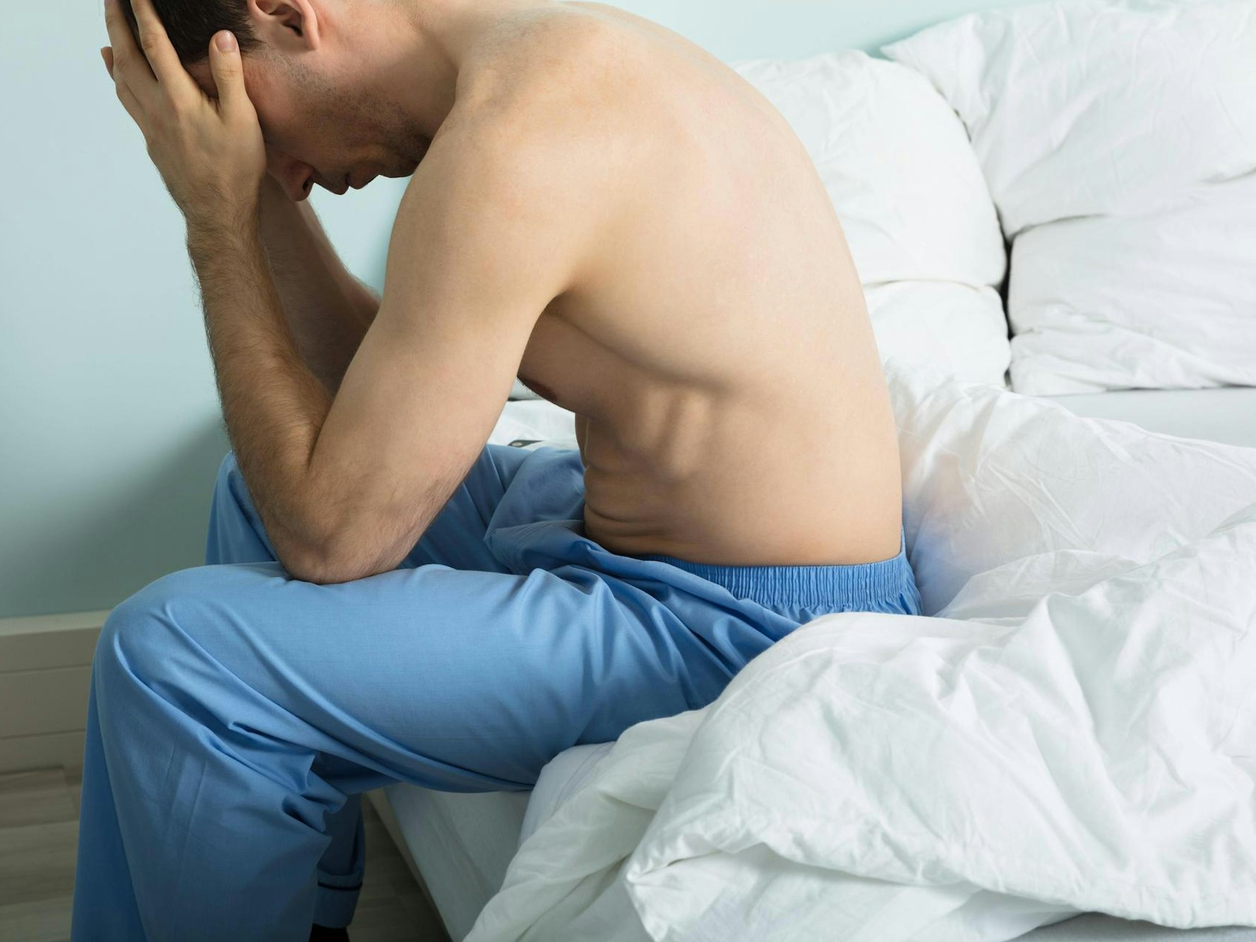 Mann sitzt auf dem Bett und zweifelt