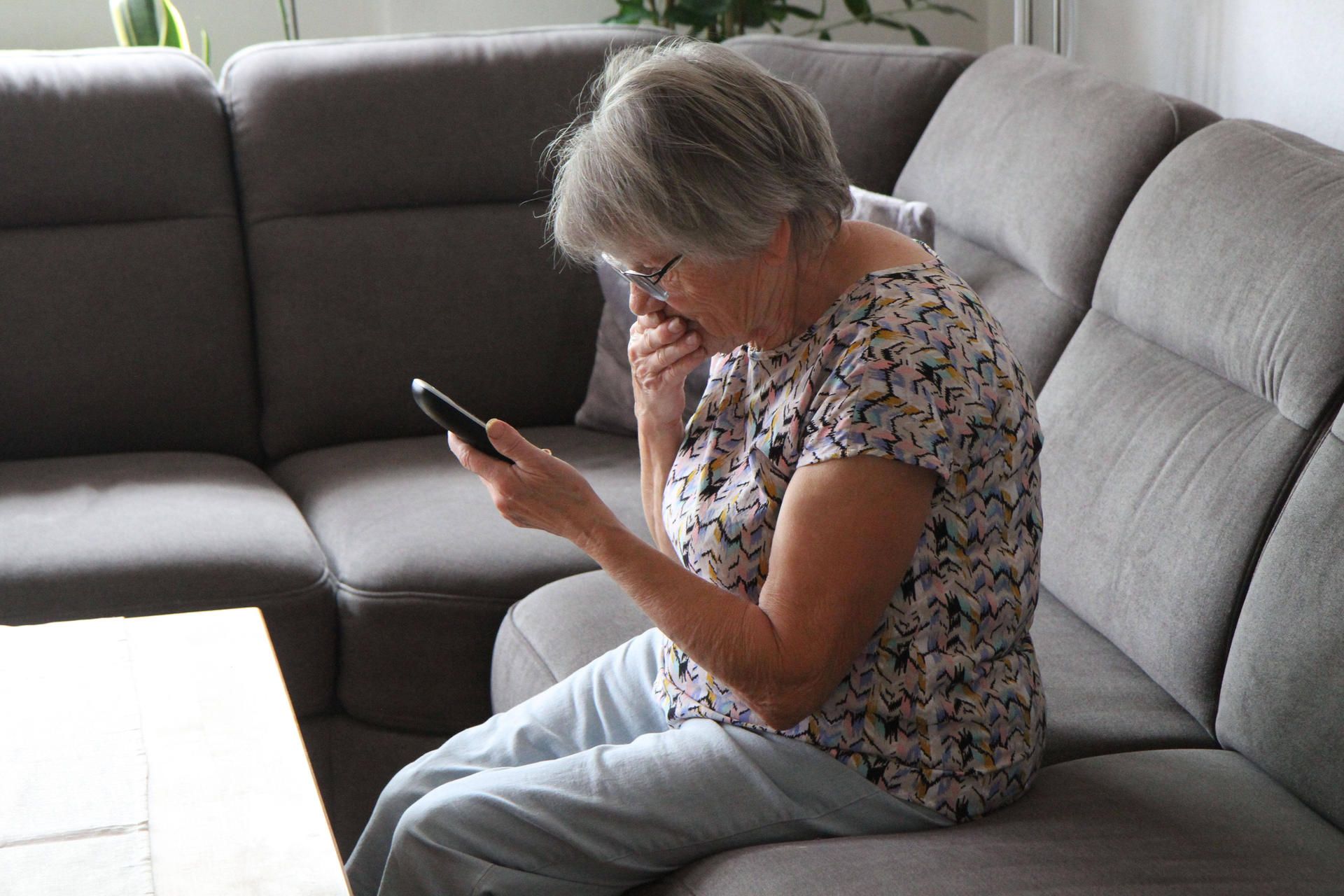 Das Foto zeigt einen schockiert wirkende Frau auf einem Sofa, die ein Telefon in der Hand hält.