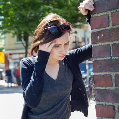 Frau hat Schwindel und hält sich an einer Hausecke fest