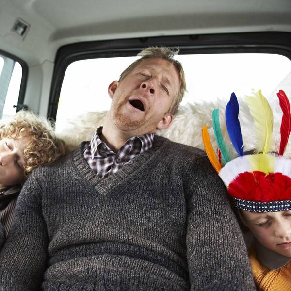 Müder Vater sitzt mit drei Kindern im Auto.