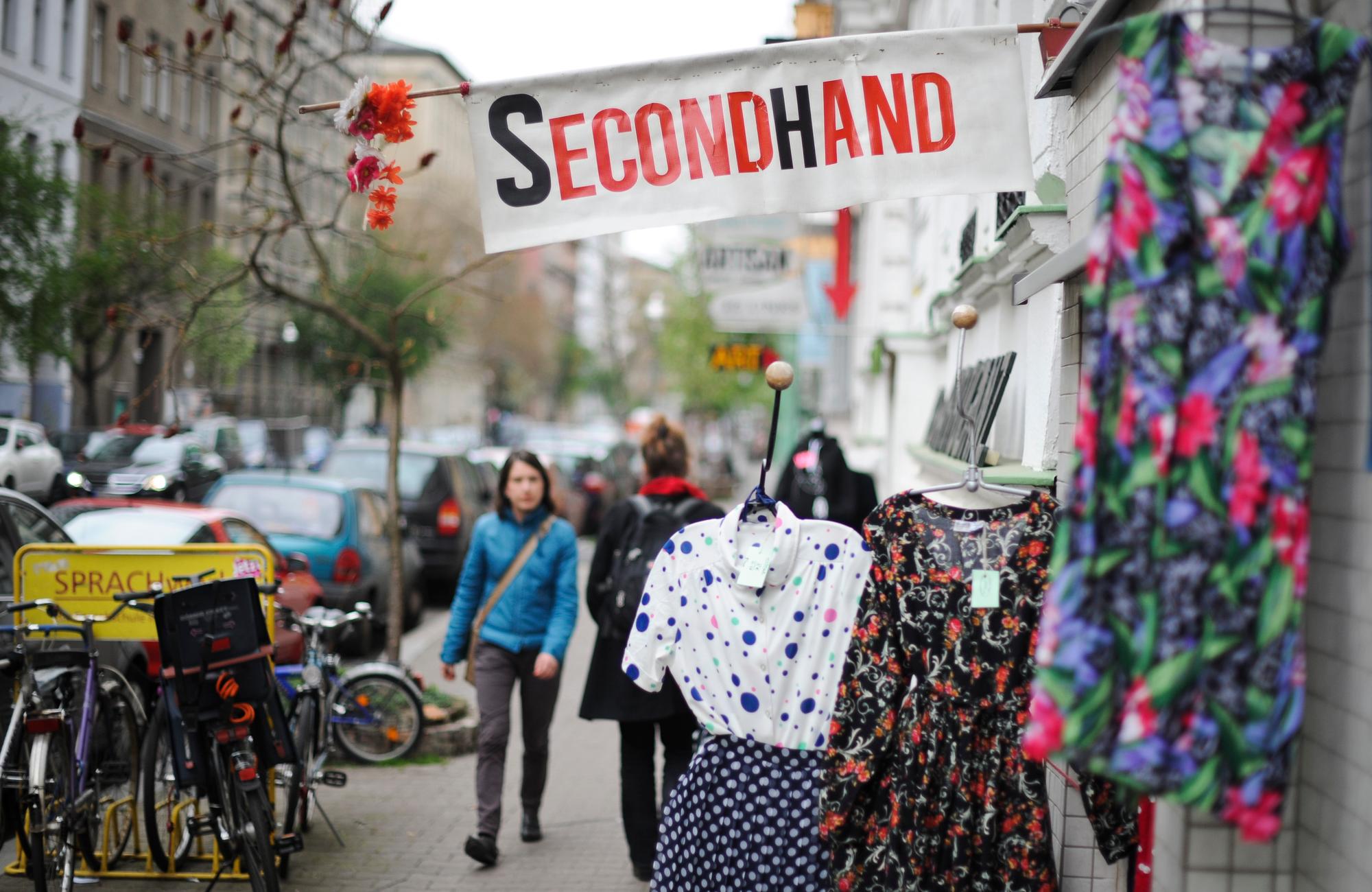 Das Schild eines Second Hand-Ladens ragt über einer Kleiderstange auf den Bürgersteig.