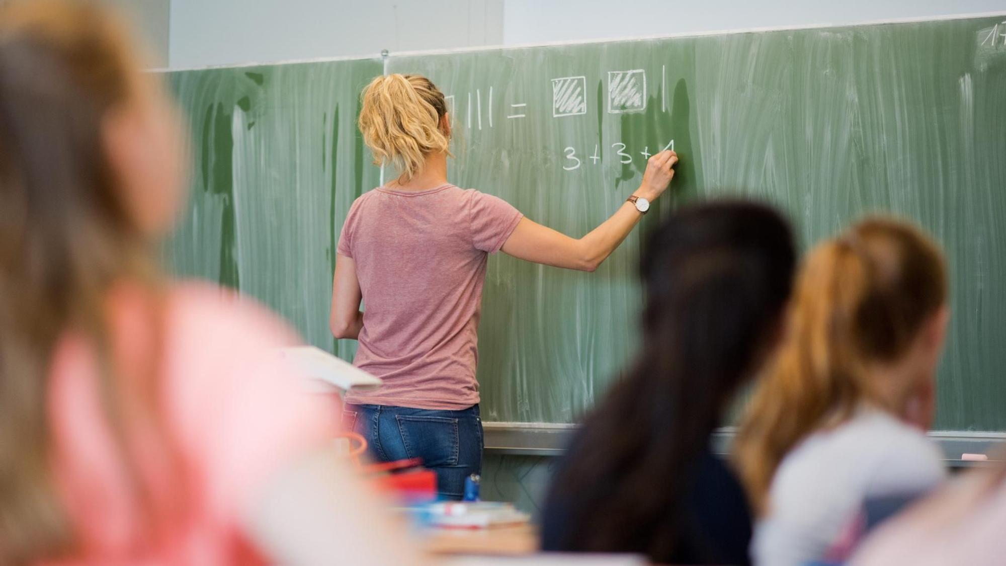 Eine Lehrerin steht an der Tafel und schreibt.