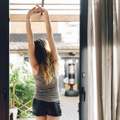 Frau streckt sich am Morgen vor Fenster