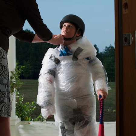 Ein Kind ist komplett mit Schutzfolie umwickelt und trägt einen Helm.