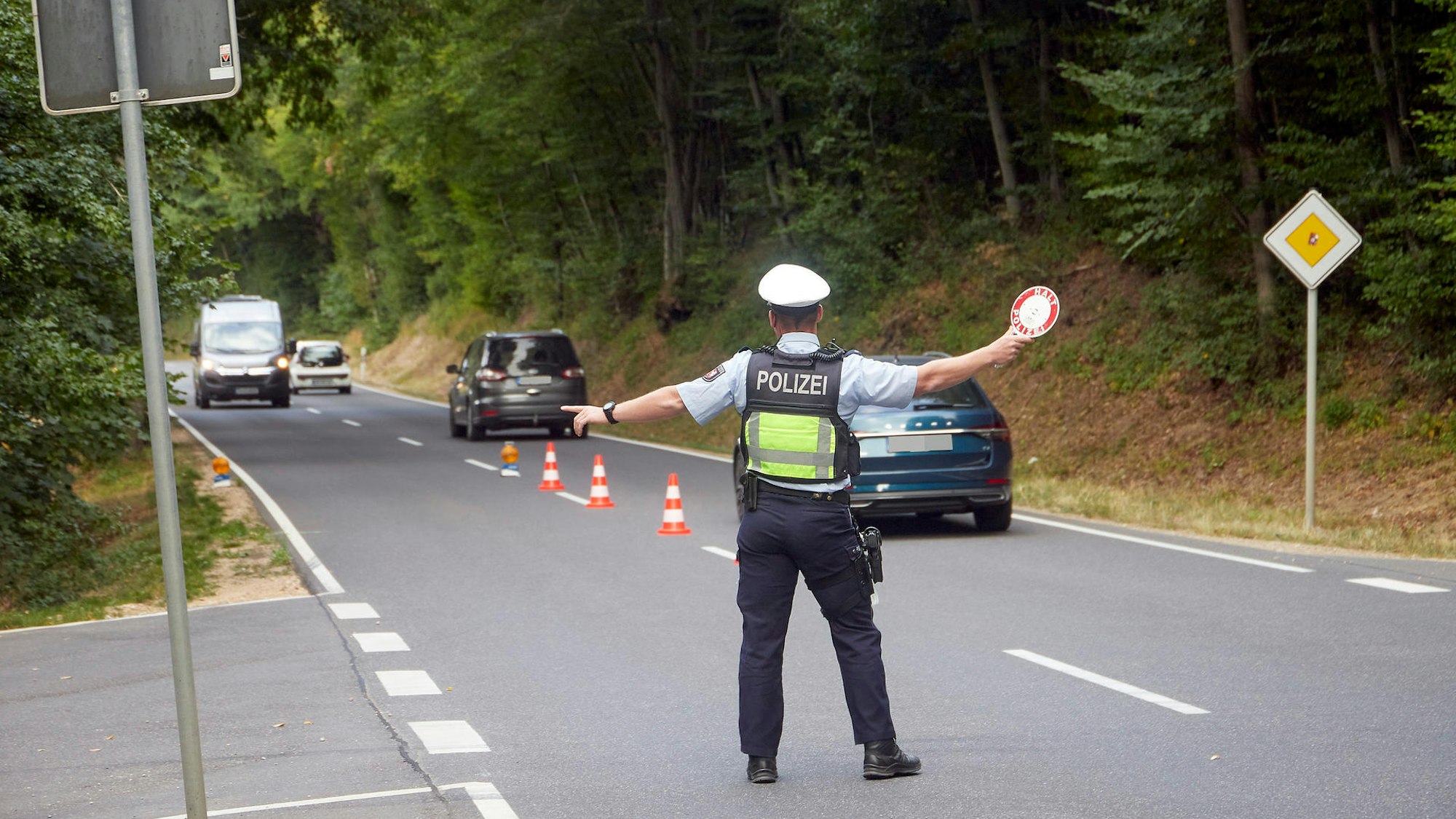 Ein Polizist hält bei einer Verkehrskontrolle eine Winkerkelle in der Hand.