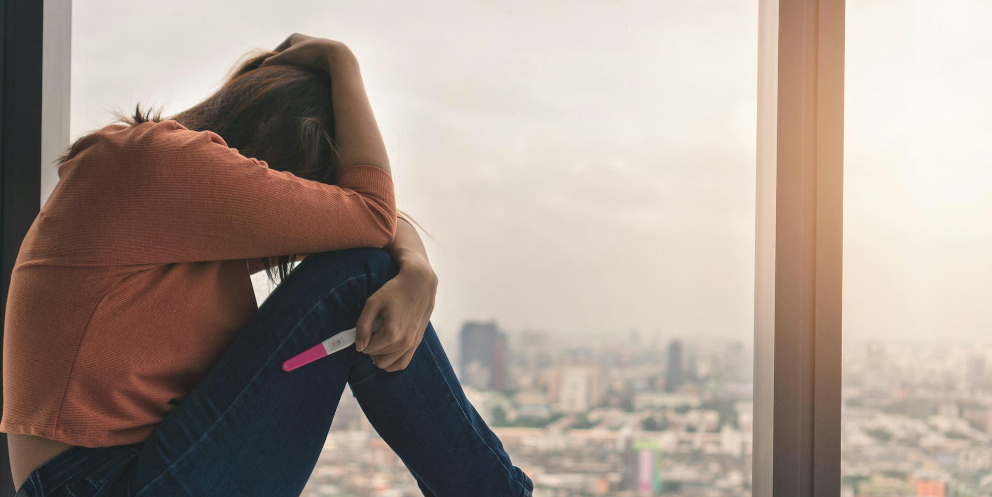 Eine Frau ist traurig und hält einen Schwangerschaftstest in der Hand.