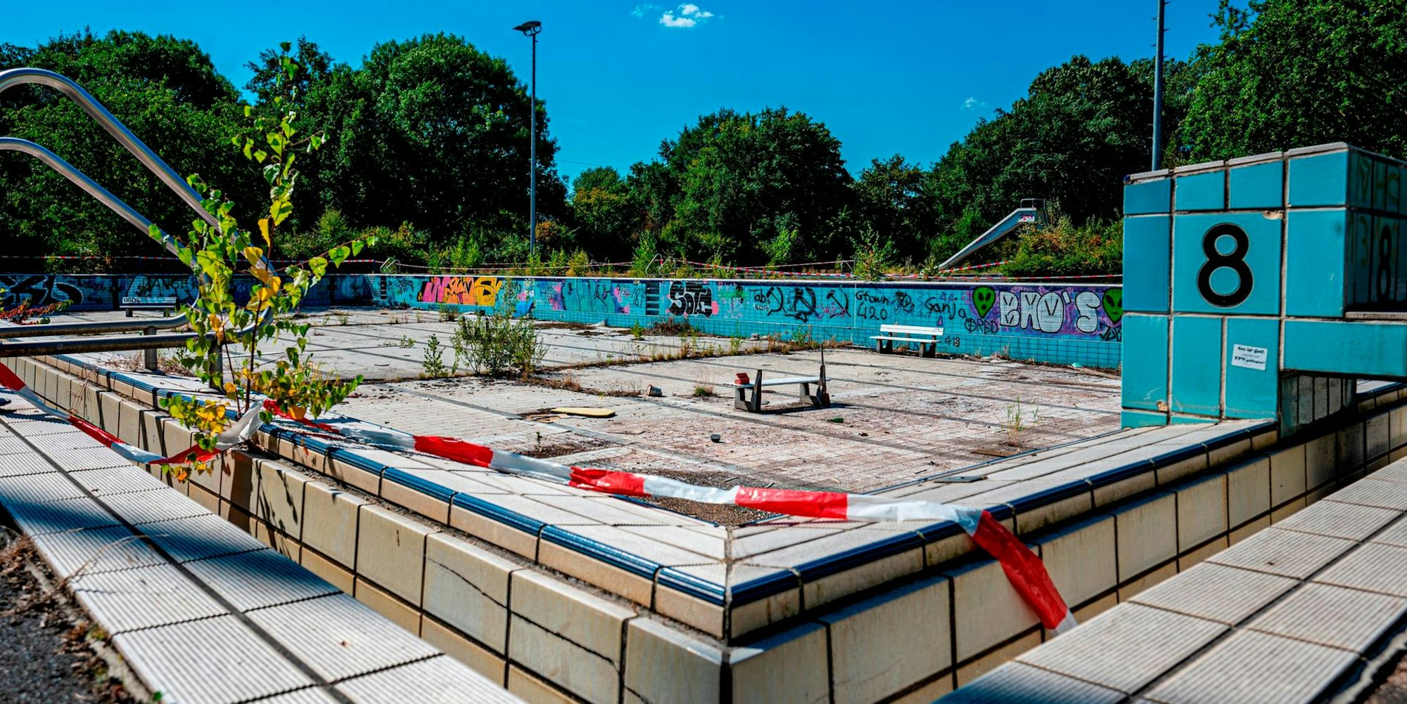 Ein verlassenes Schwimmbecken ohne Wasser. Über dem Rand liegt Absperrband.