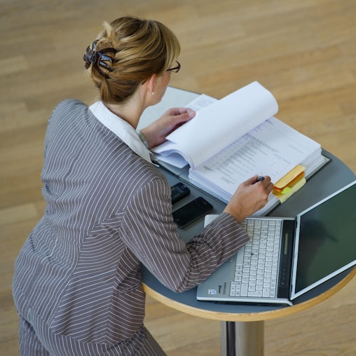Frau steht an Stehtisch und arbeitet